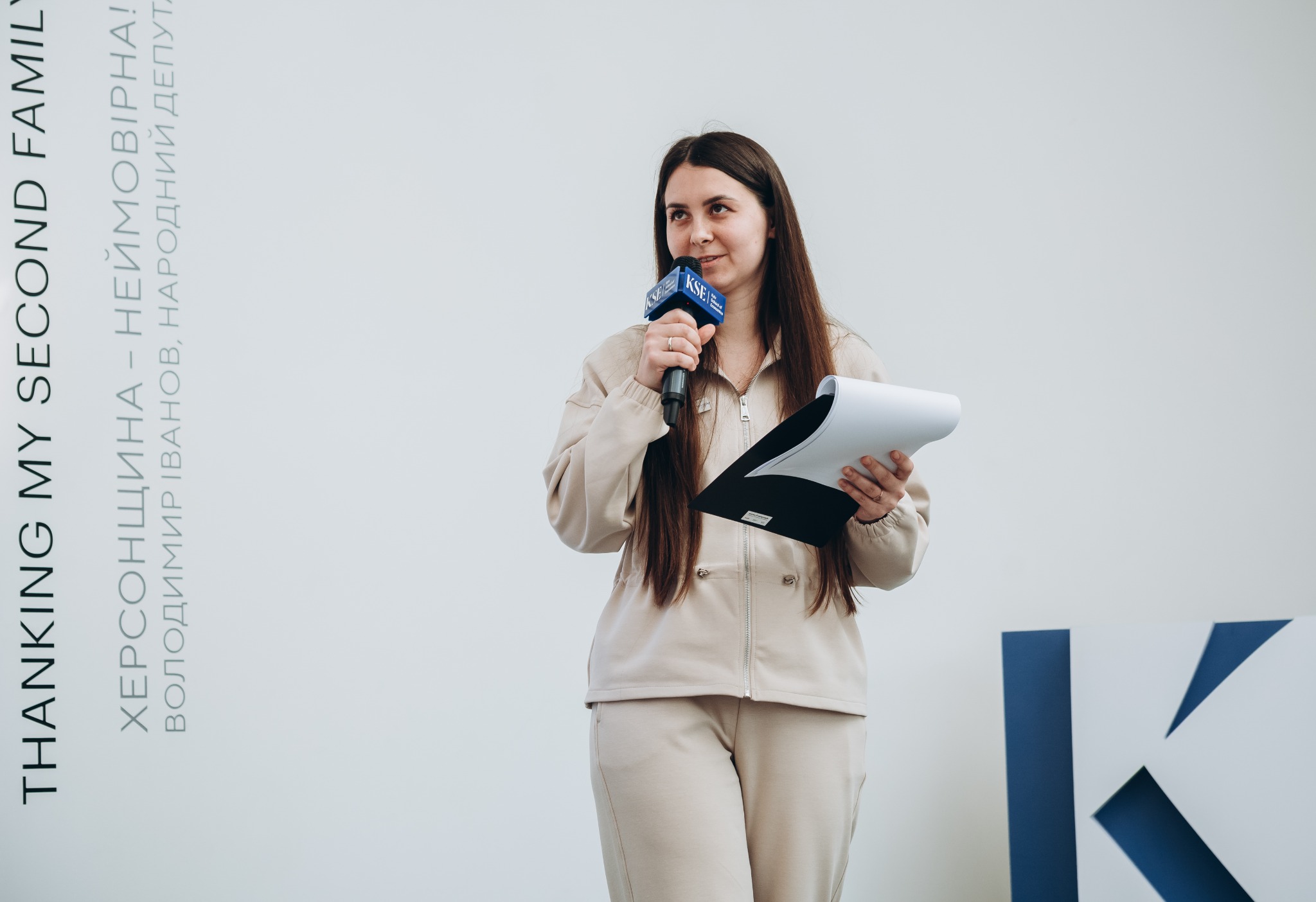 Жінка виступає з мікрофоном KSE та тримає папери.